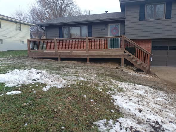 Gray house with wooden deck and stairs. Snow on the lawn.