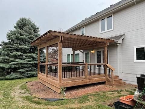 Wooden deck with a covered pergola attached to a light-colored house. Dark railing, overcast sky.