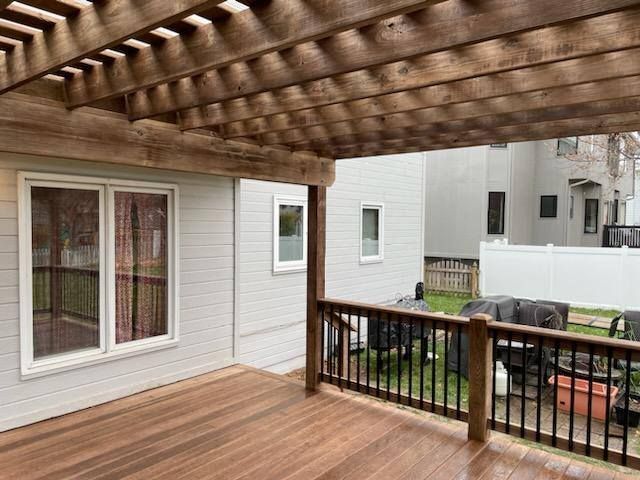 Wooden deck with pergola, looking into a backyard with a white house and fence.