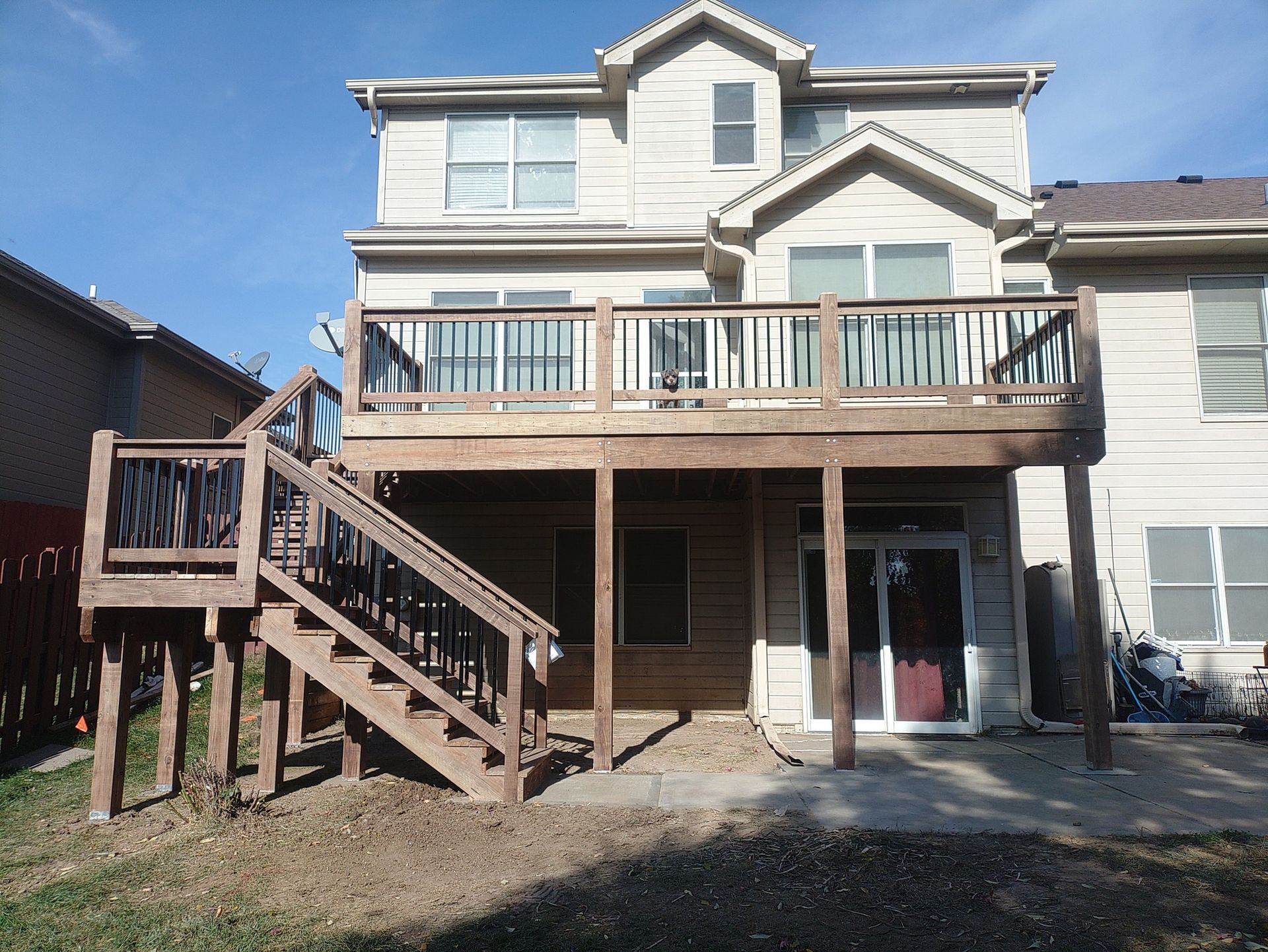 Two-story house with dark blue siding and a brown deck, stairs, and railing.