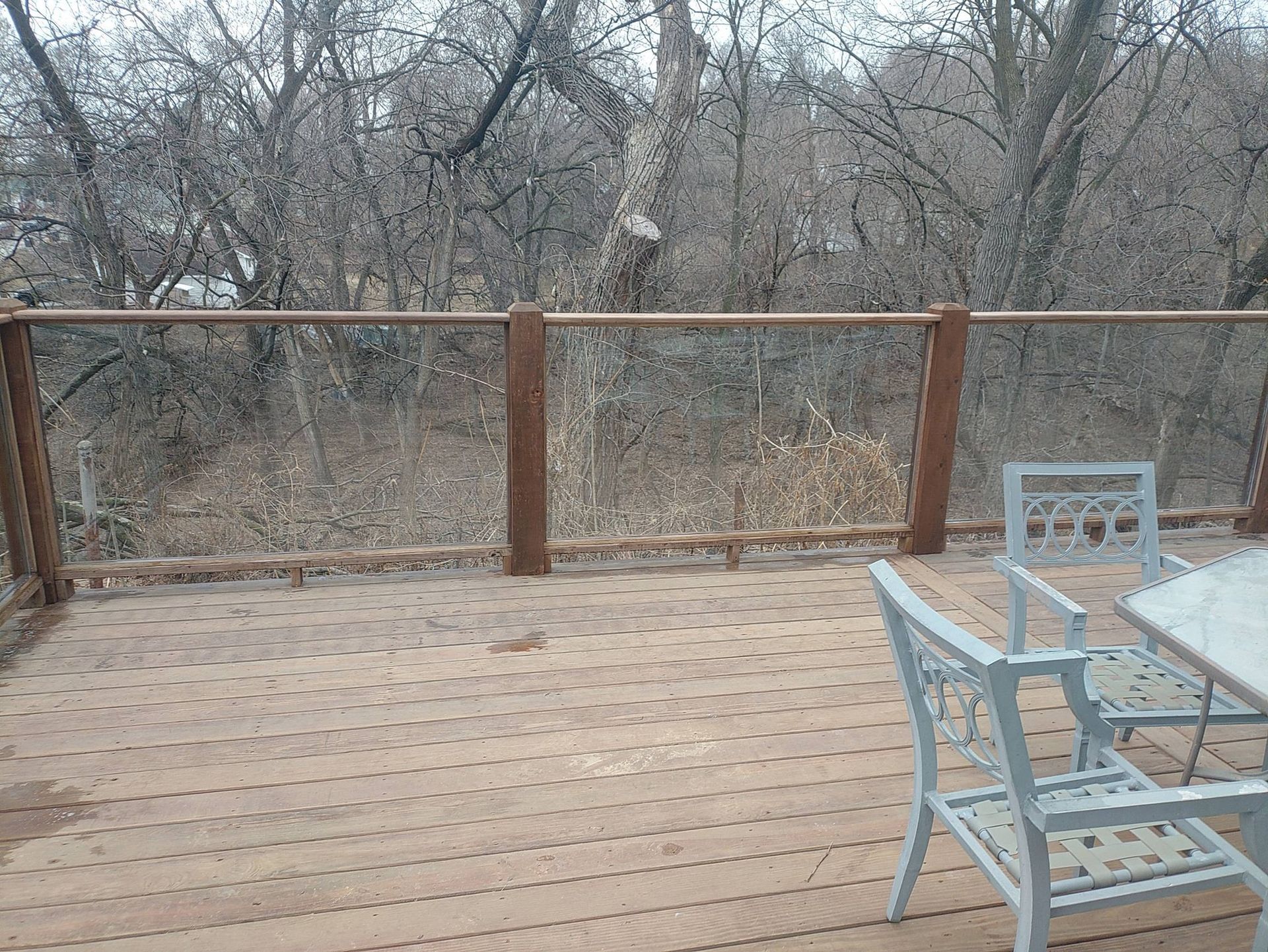 Deck with stairs in front of a gray house; patches of snow on the ground and brown and green grass.