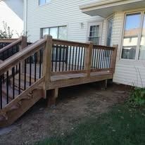 Wooden deck with black railing next to a house with beige siding and windows.