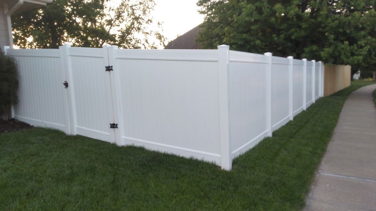 White vinyl fence with gate surrounding a green lawn next to a sidewalk.