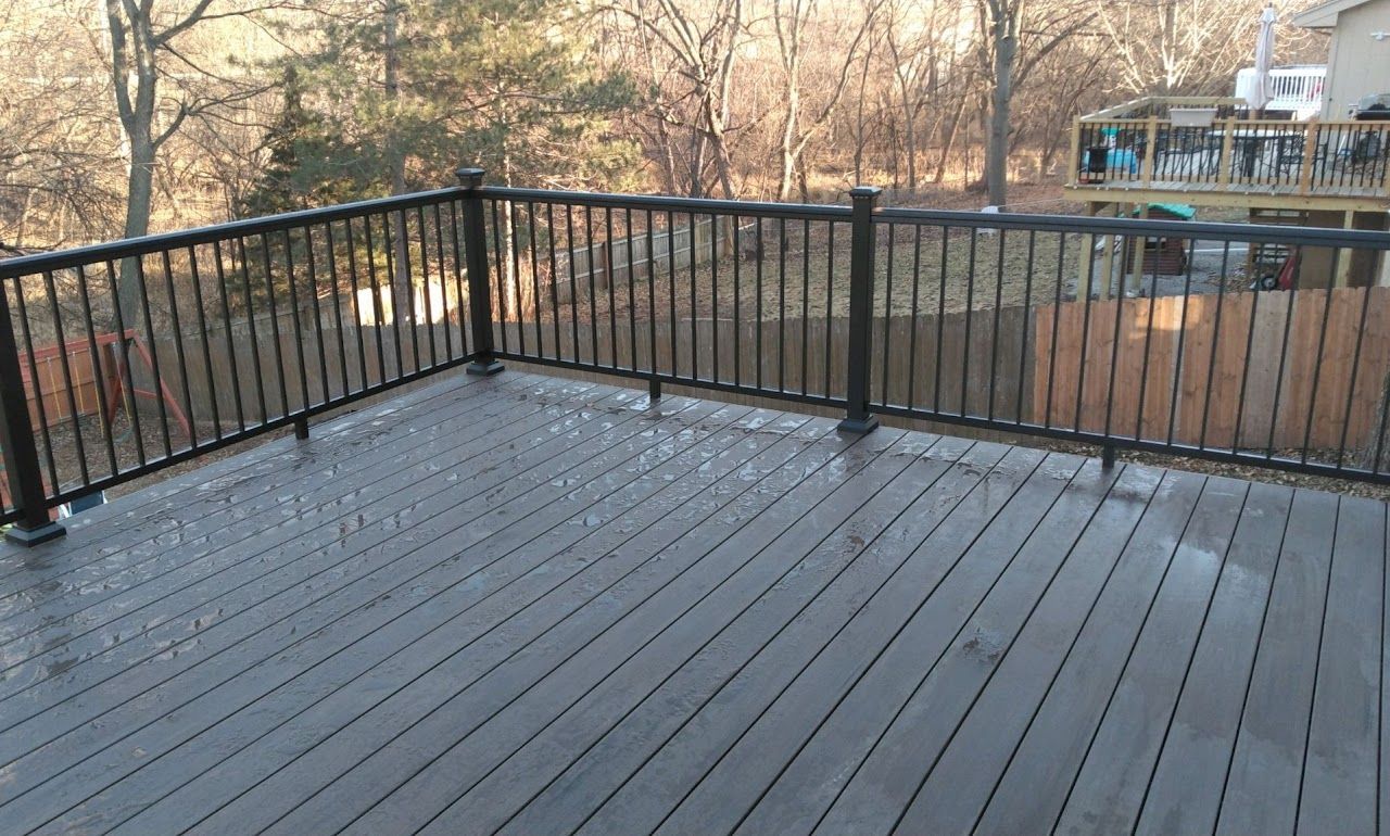 Gray deck with black railing overlooking a wooded area.