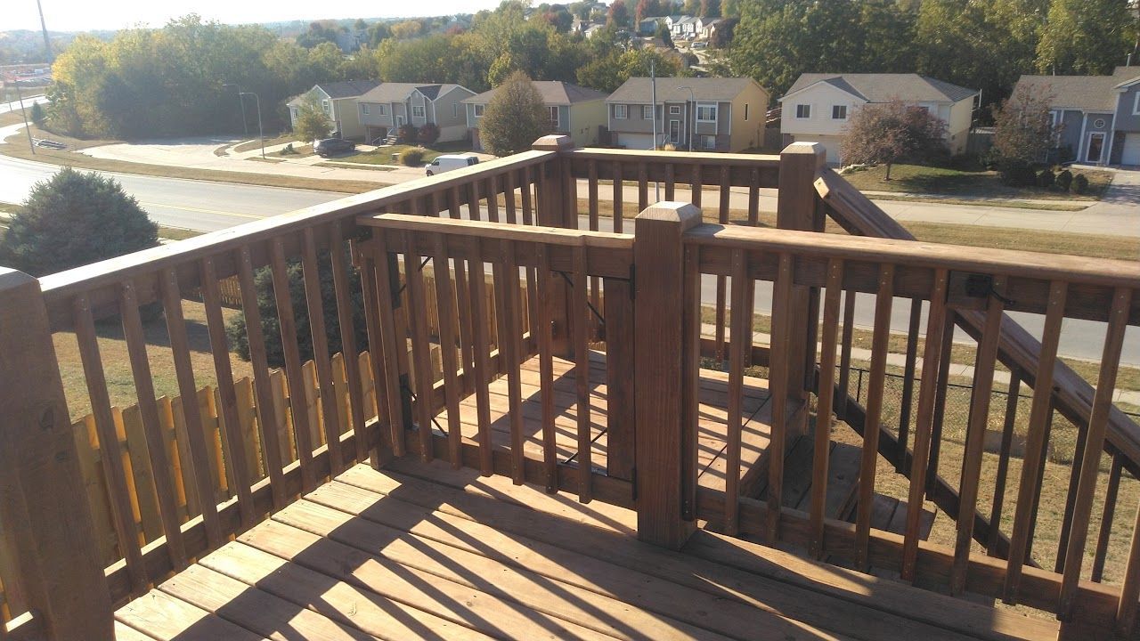 Wooden deck railing with view of street and houses on a sunny day.