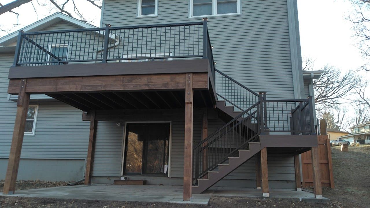 Two-story wooden deck with dark railing and stairs attached to a gray house.