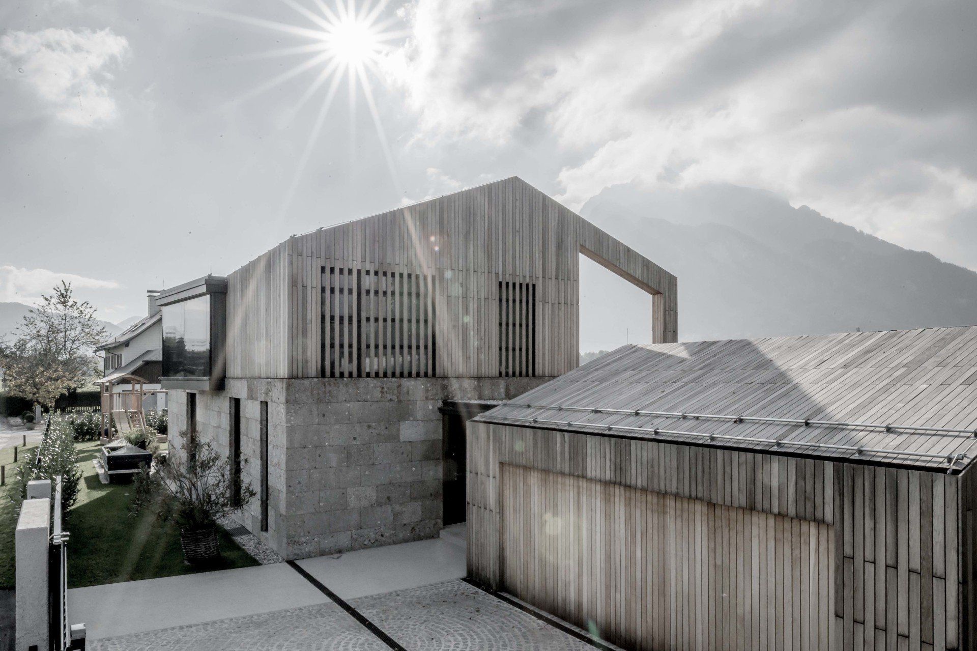 Ein Schwarzweißfoto eines Hauses, bei dem die Sonne durch die Wolken scheint.