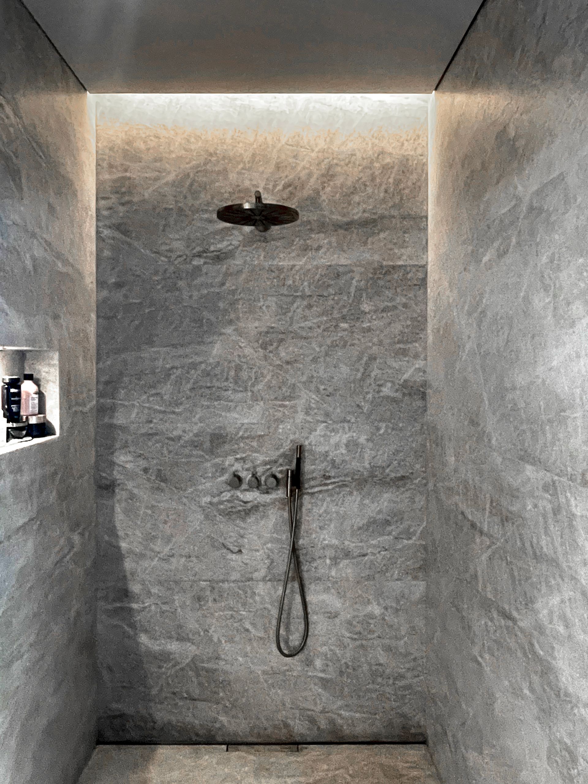 Eine Dusche mit einem Duschkopf und einem Schlauch in einem Badezimmer.