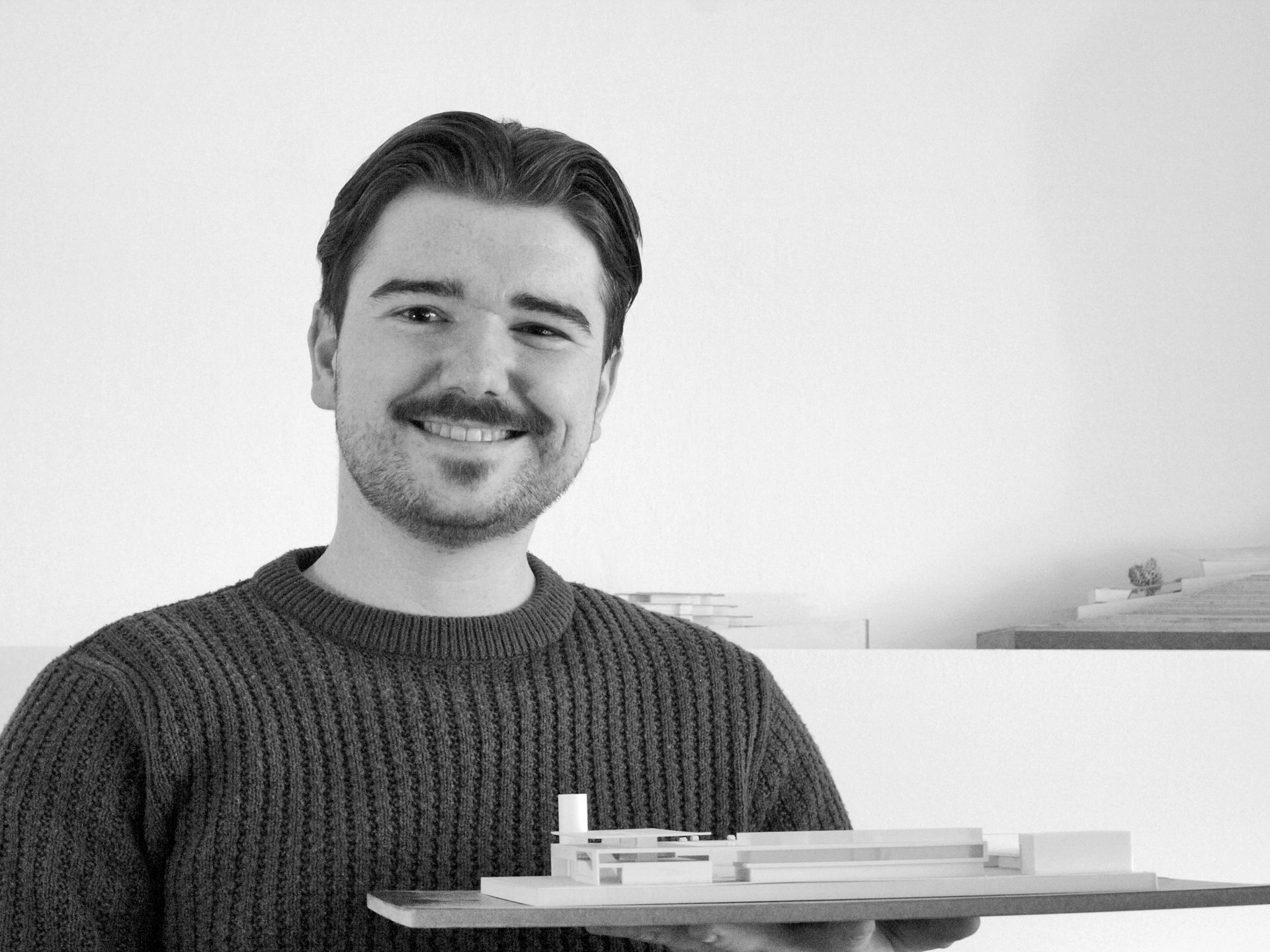 Ein Mann im Pullover hält ein Gebäudemodell in der Hand.