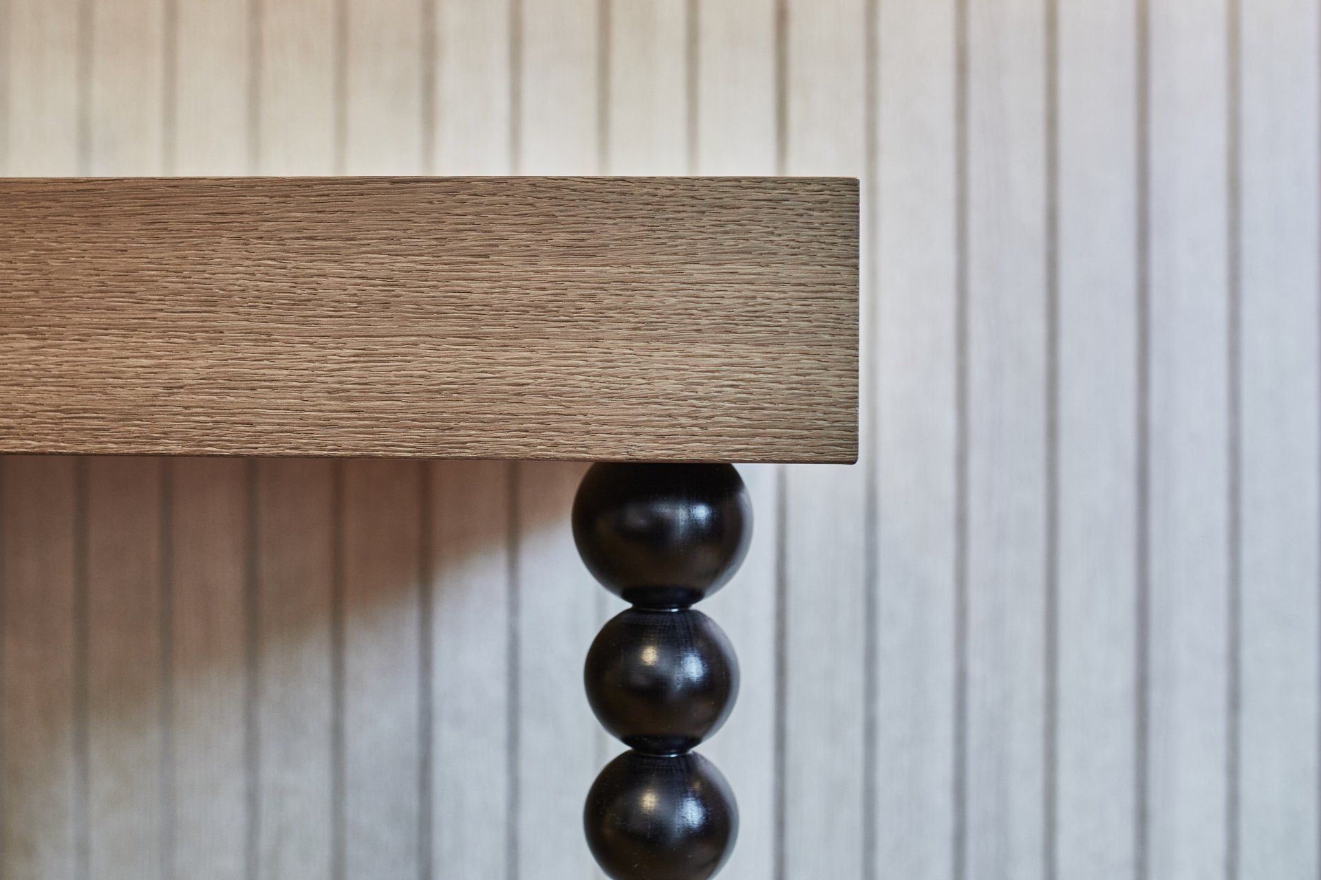 Ein Holztisch mit drei schwarzen Perlen an den Beinen steht vor einer weißen Wand.