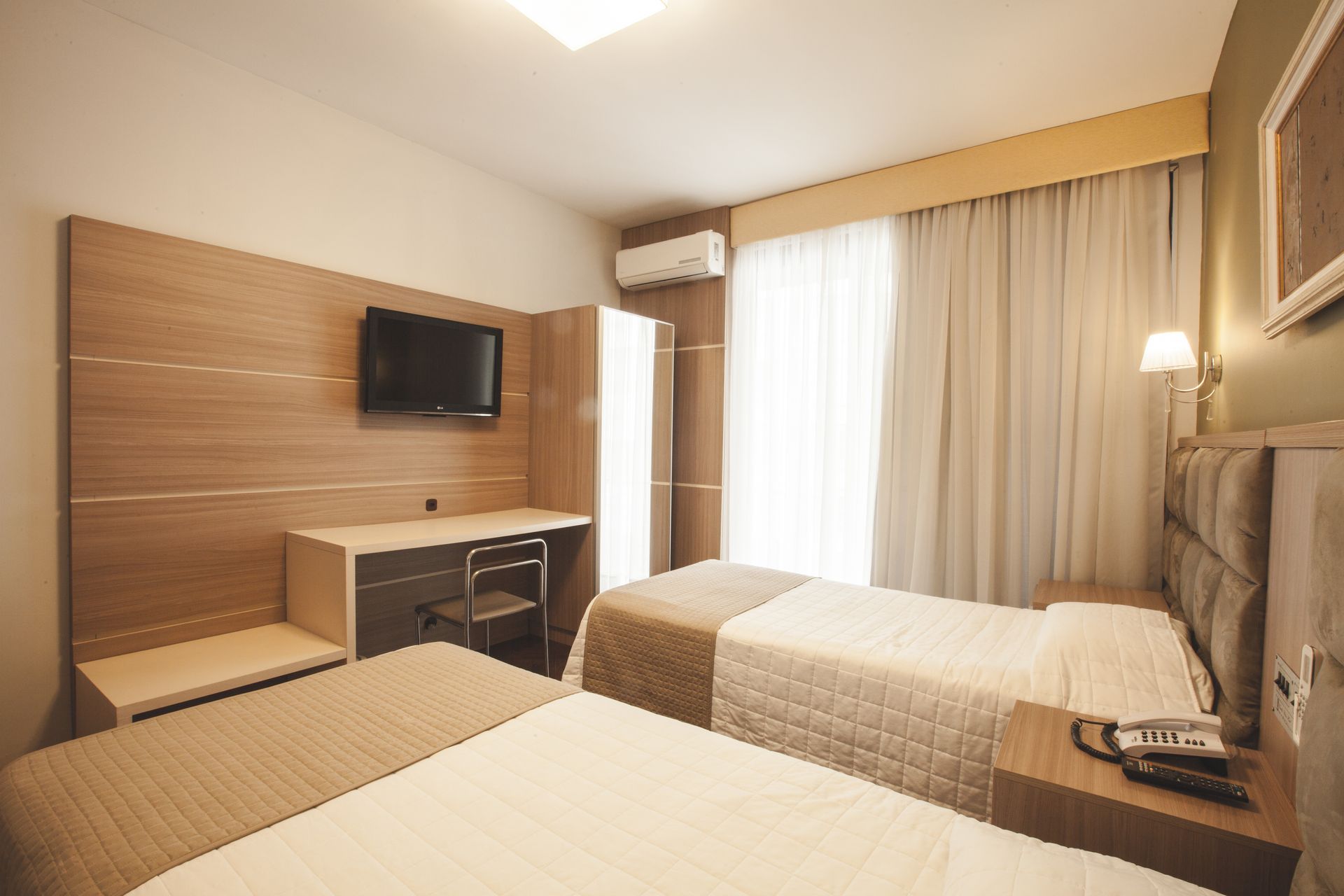 Um quarto de hotel com duas camas, uma mesa e uma TV de tela plana.