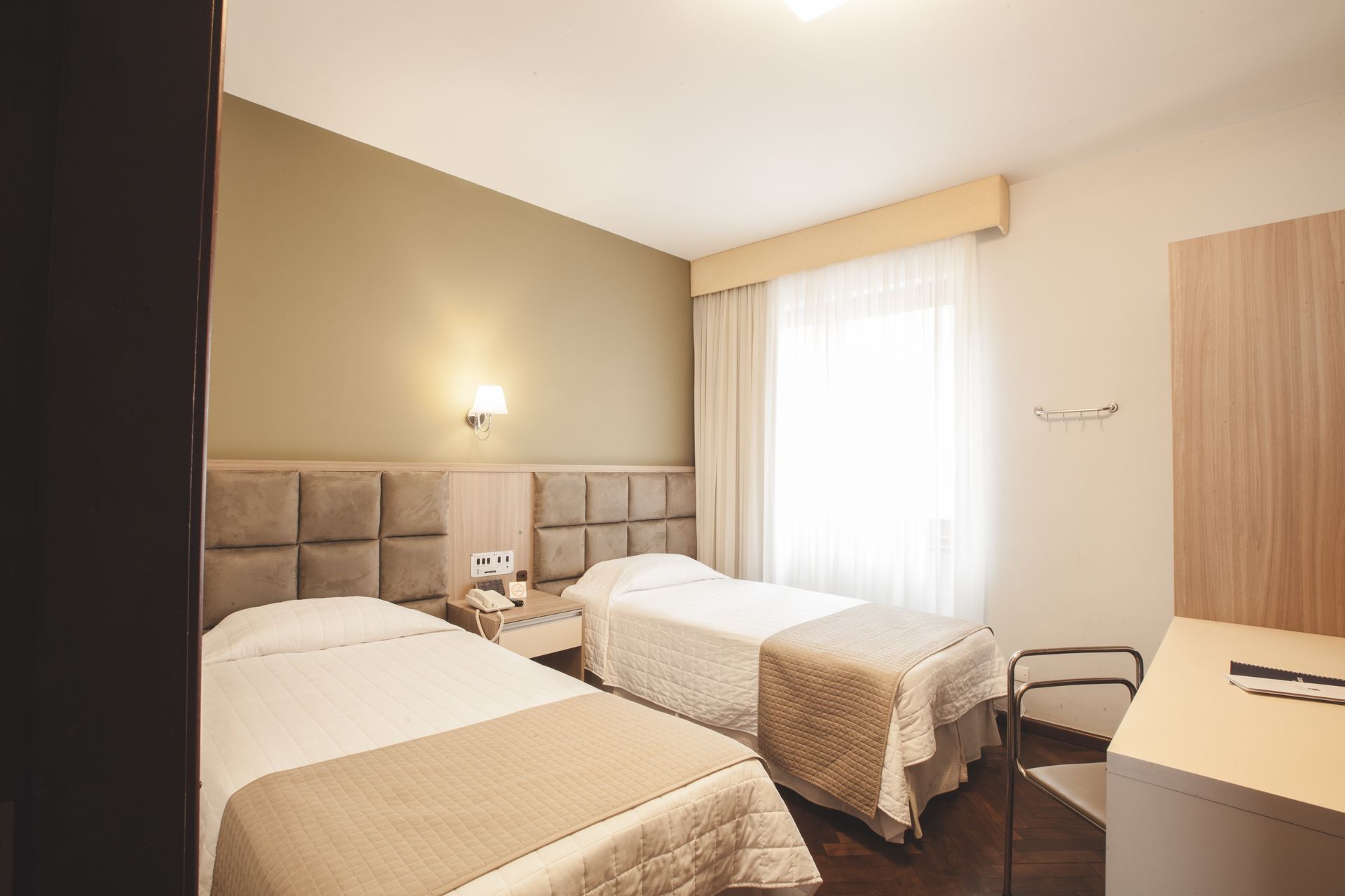 Um quarto de hotel com duas camas, uma escrivaninha e uma janela.