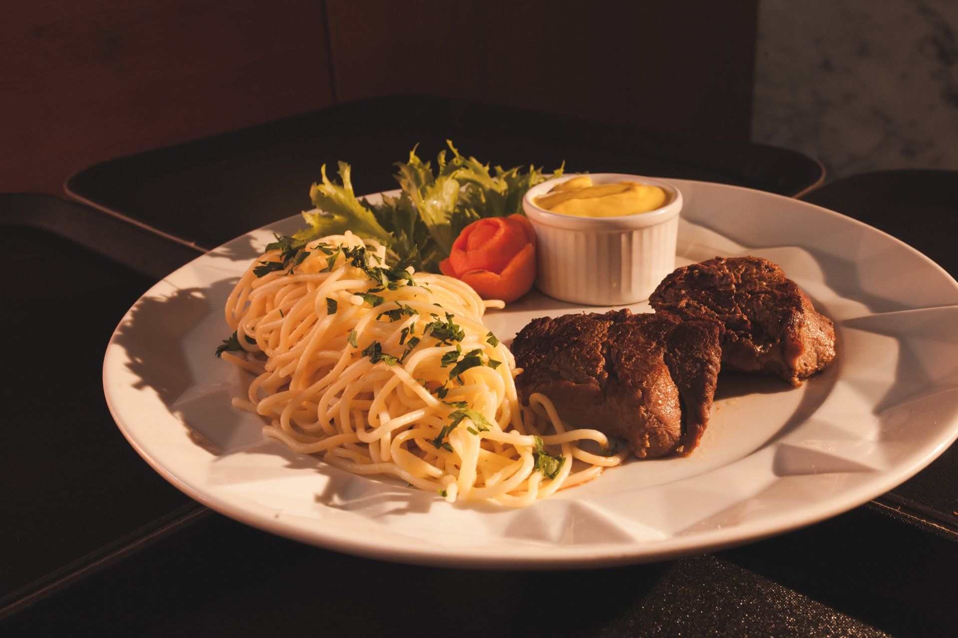 Um prato branco coberto com espaguete, almôndegas e legumes.