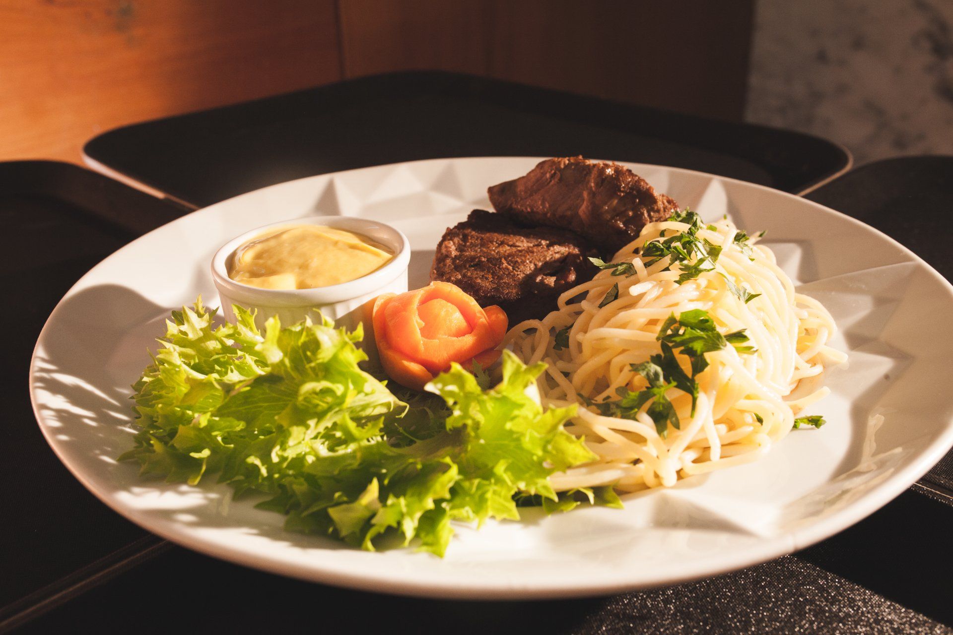 Um prato de comida com macarrão, carne e alface sobre uma mesa.