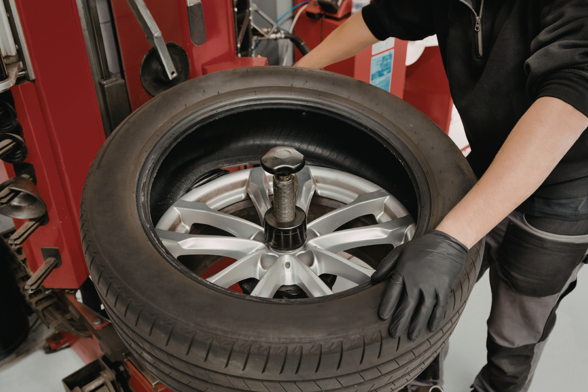 Mechanic mounting a tire on a machine in a shop; hands in black gloves.