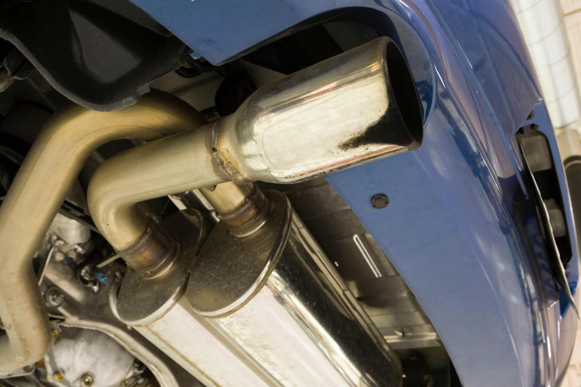 Close-up of a blue car's chrome exhaust pipe, angled view from below.