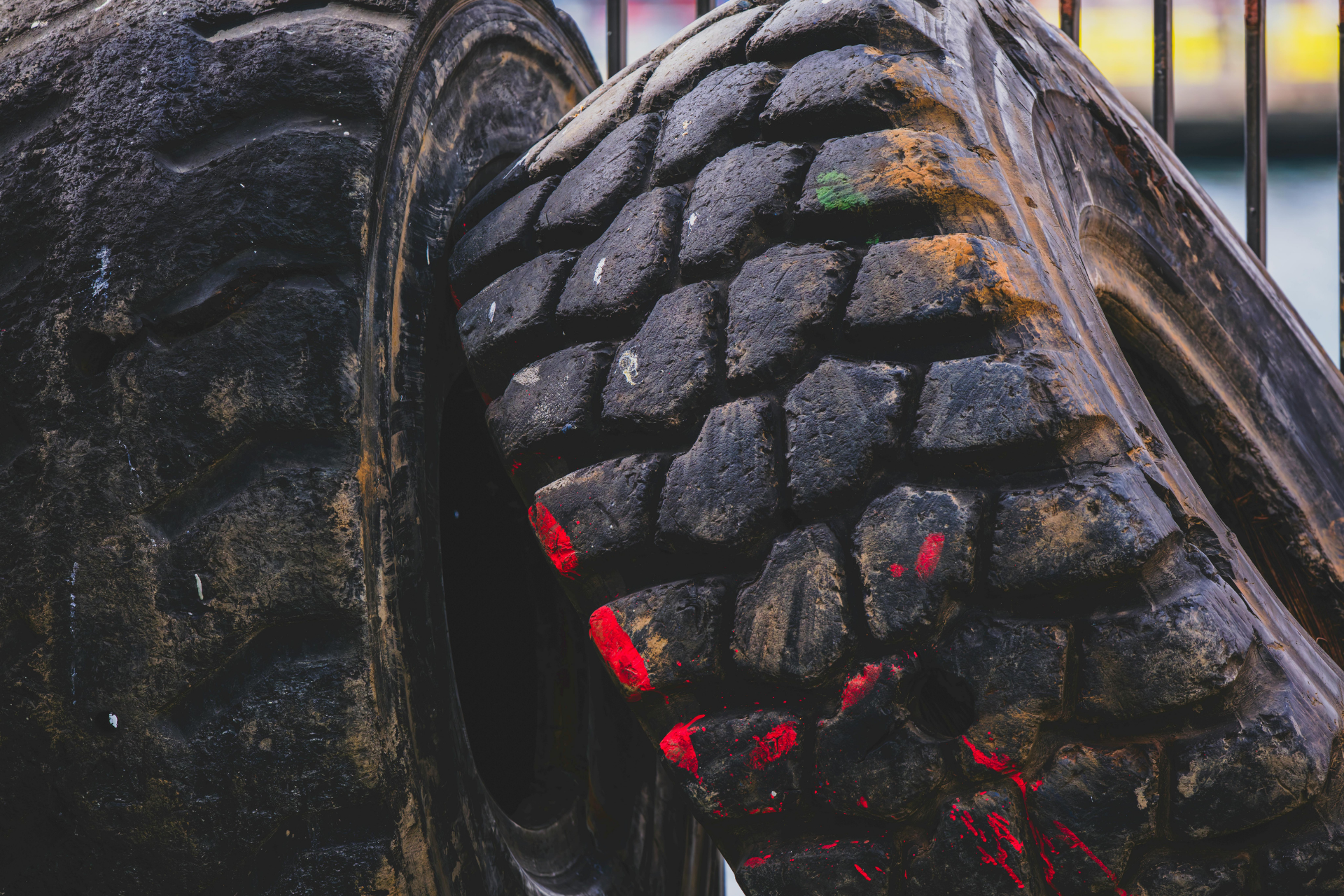 Old, worn, black tires with textured treads. Red and green paint marks. Near a fence.