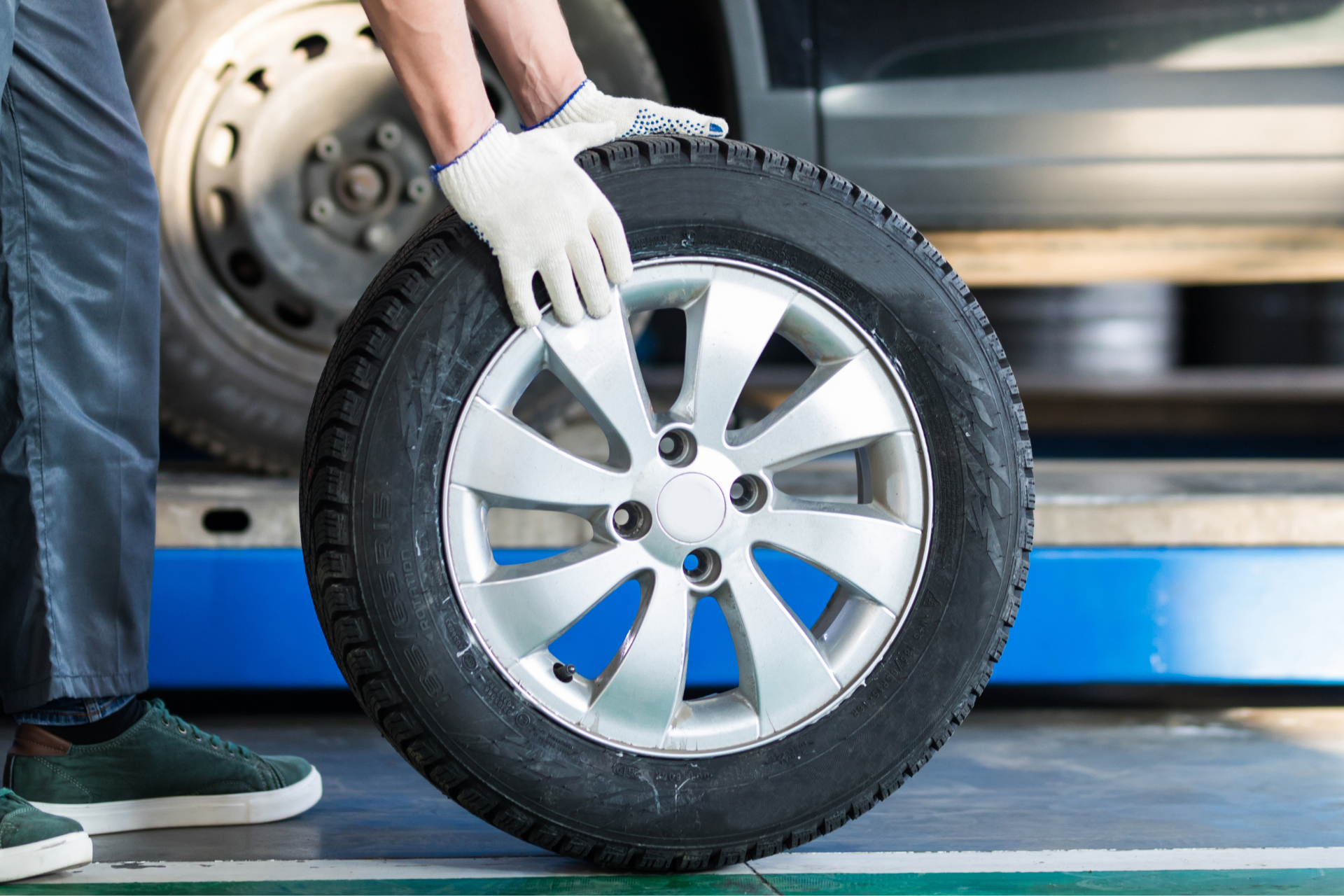 Person in work gloves holding a car tire next to a vehicle.