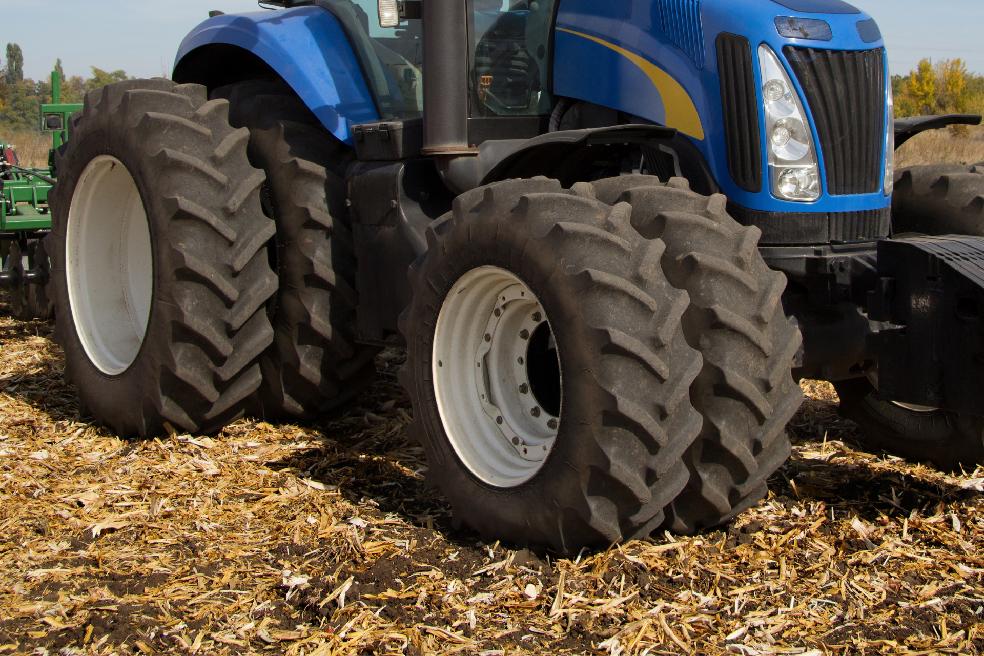 Blue tractor with large tires working in a field of harvested corn.