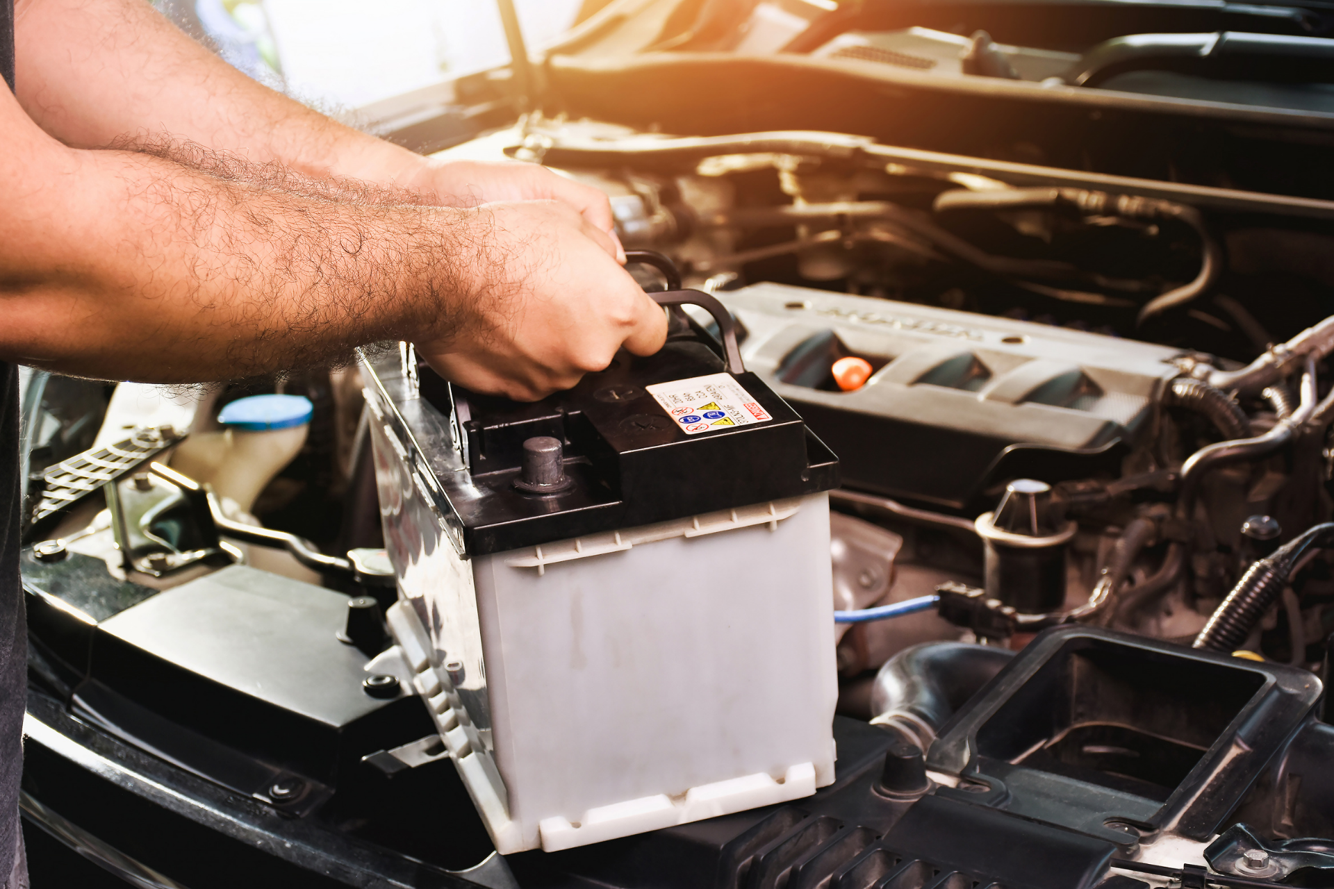 Person testing a car battery in a garage with a diagnostic tool. Blue car and battery are visible.