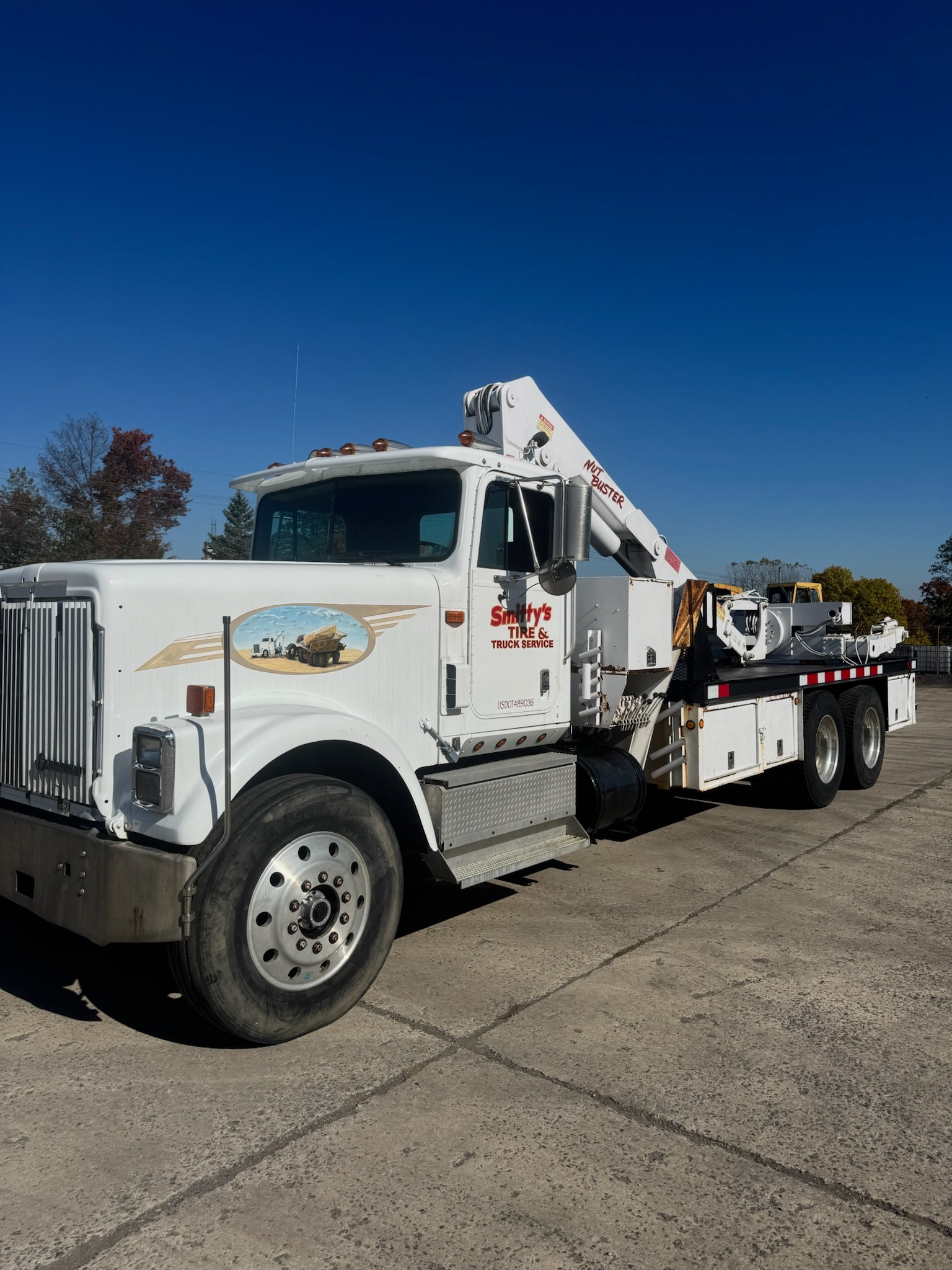 White truck with crane on a concrete surface against a blue sky.