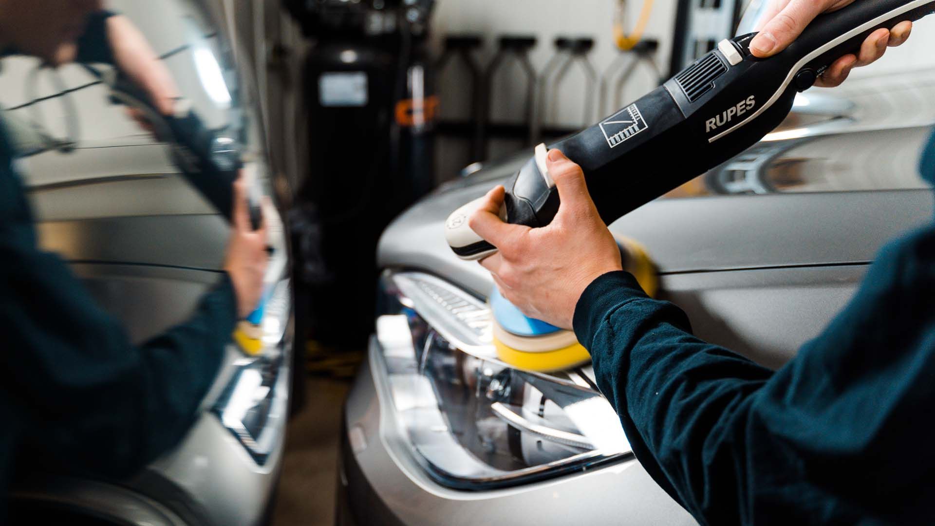 Person polishing a car headlight with a power polisher, in a garage setting.