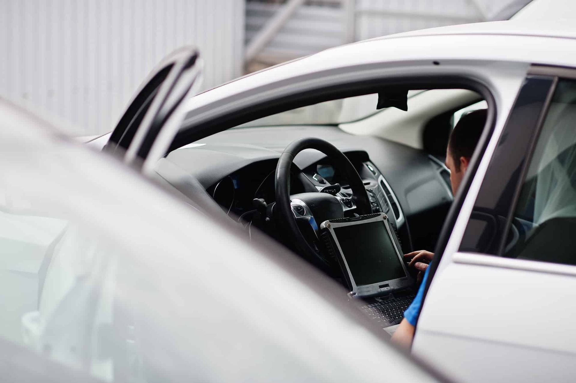 Person using a tablet inside a white car with the door open, likely for diagnostics.