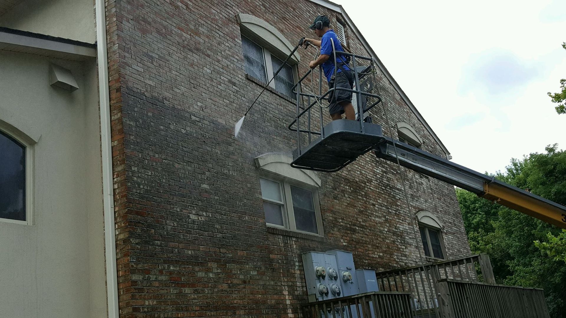 A man is cleaning a brick building with a high pressure washer.