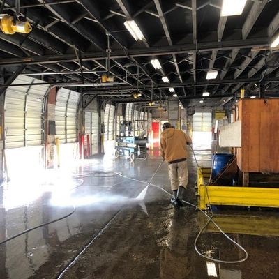 A man is using a high pressure washer to clean a warehouse floor