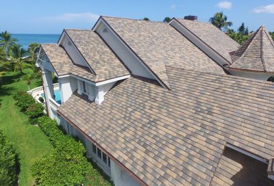 An aerial view of a large house with a roof overlooking the ocean.