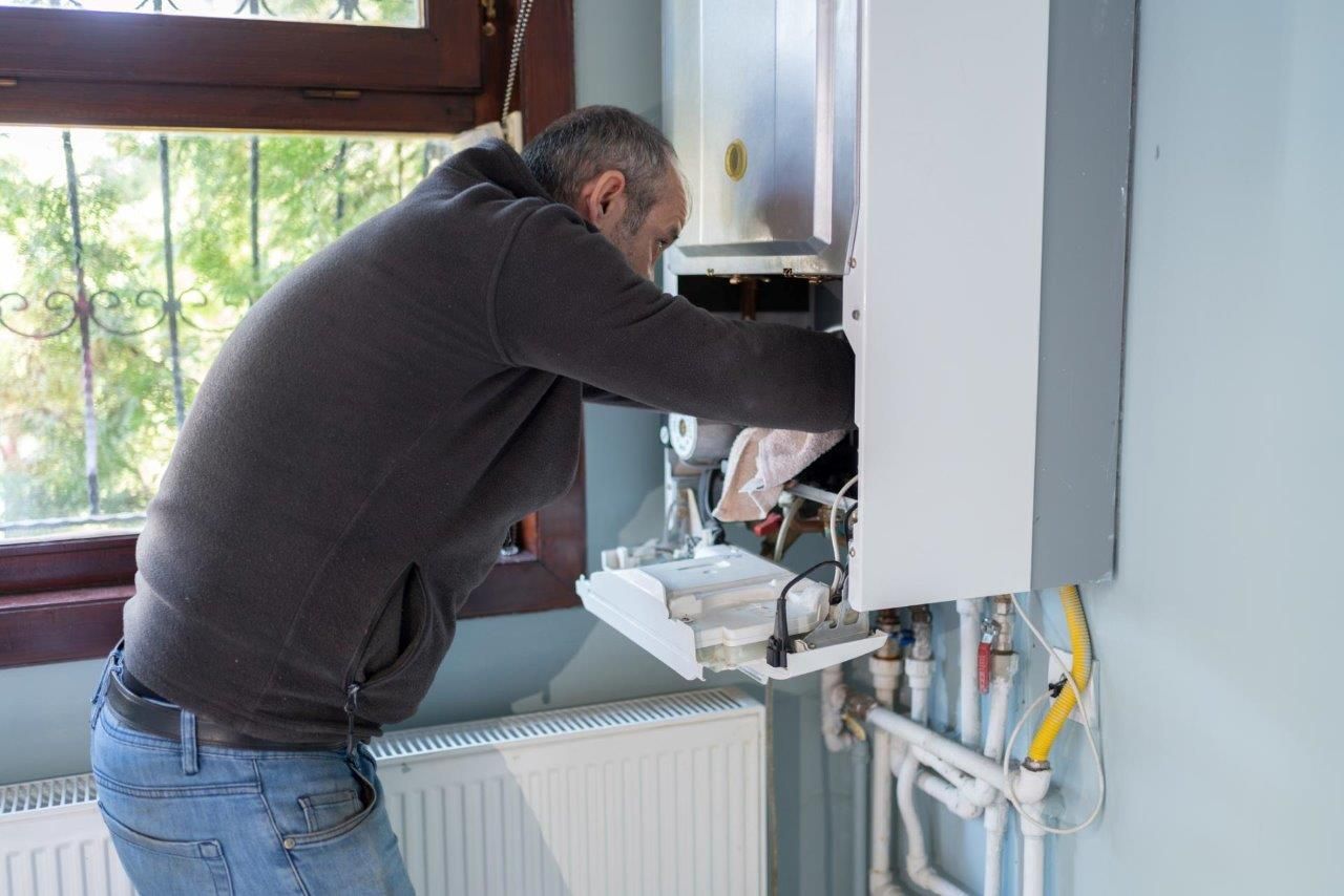 Un uomo sta riparando una caldaia con un cacciavite.