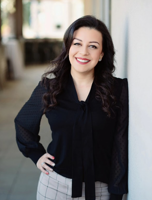 A woman in a black shirt is leaning against a wall and smiling.