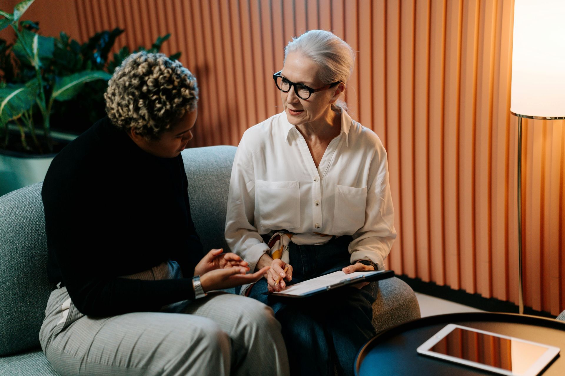Two women are sitting on a couch talking to each other.
