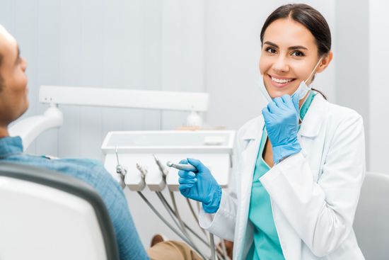A dentist smiling beside a patient in a chair, tools ready in a bright clinic setting.