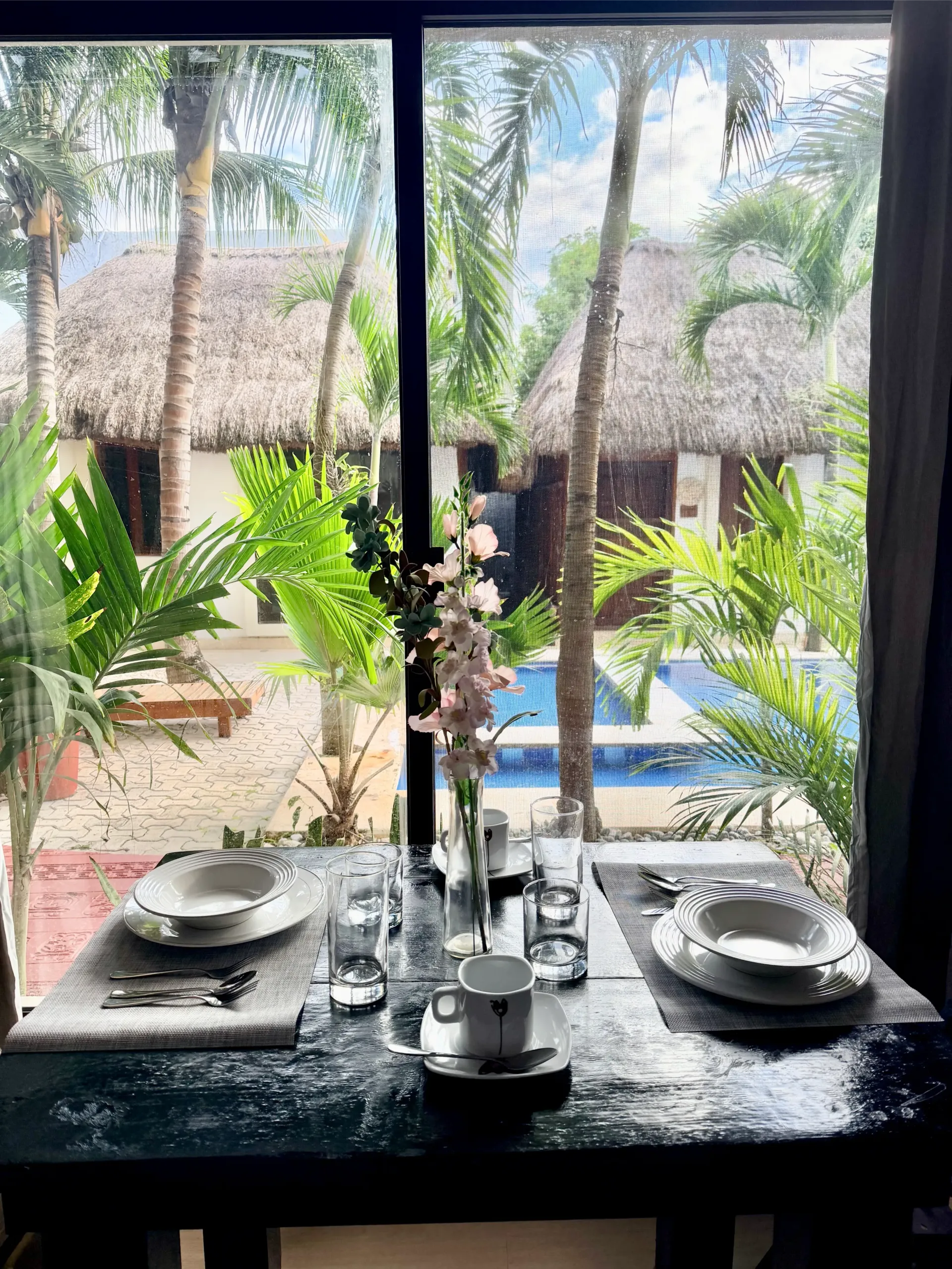 Modern living room with large sliding glass doors open to an outdoor dining area. Features include a grey sofa, fireplace, and wood and brick accents.