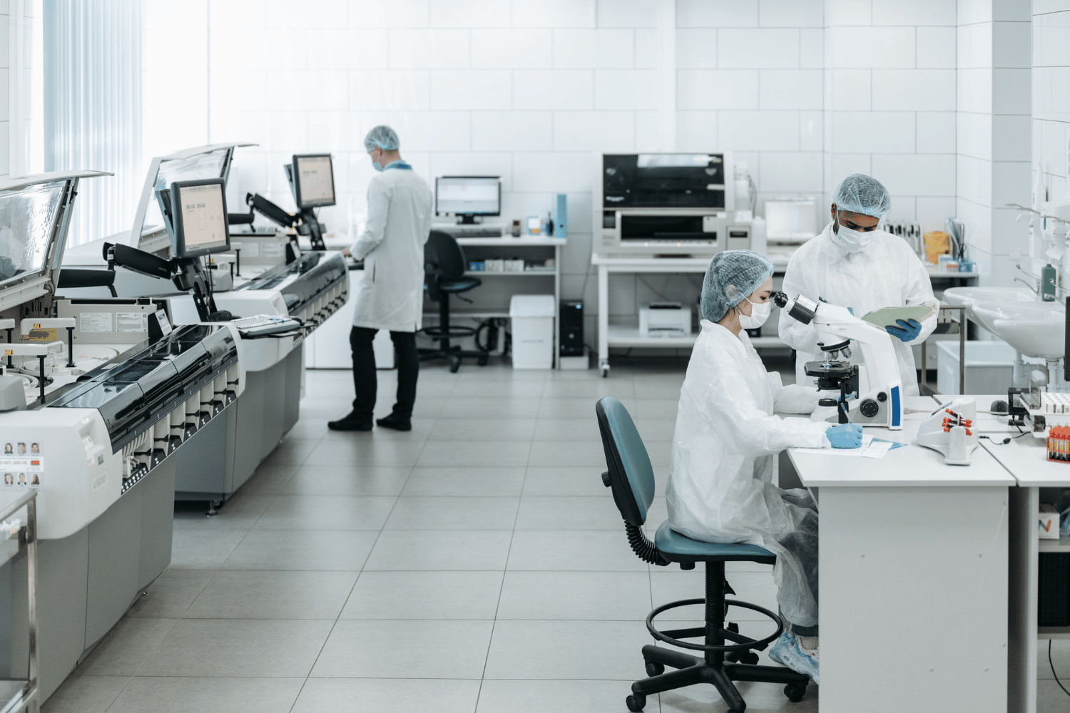 Laboratory technicians in white coats working with microscopes and computer equipment