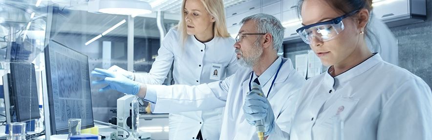 Scientists in lab coats analyze data on a computer screen in a modern laboratory setting.