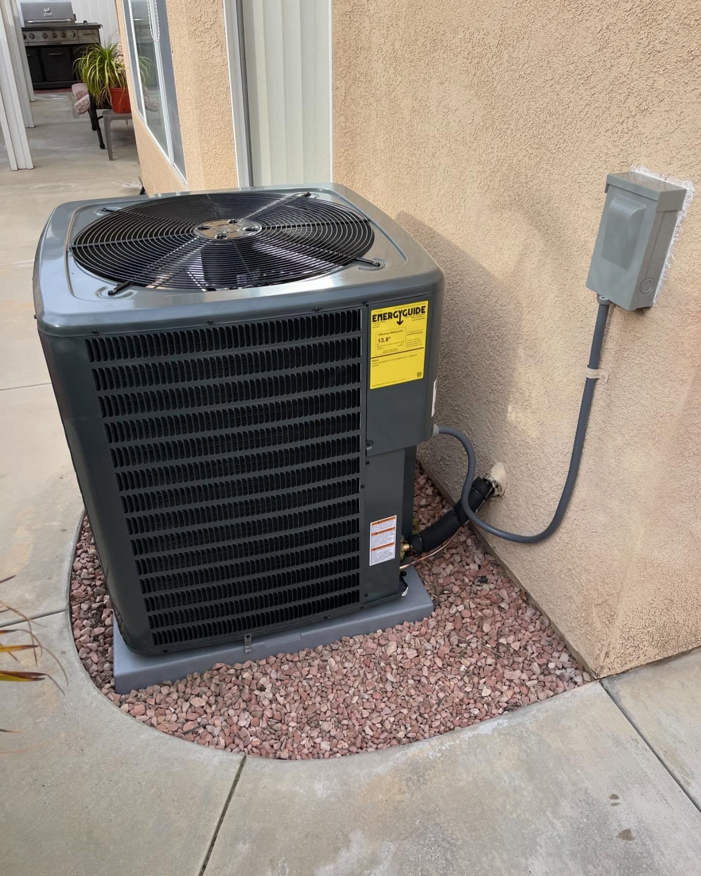 Gray air conditioning unit outside a beige house, set on gravel.
