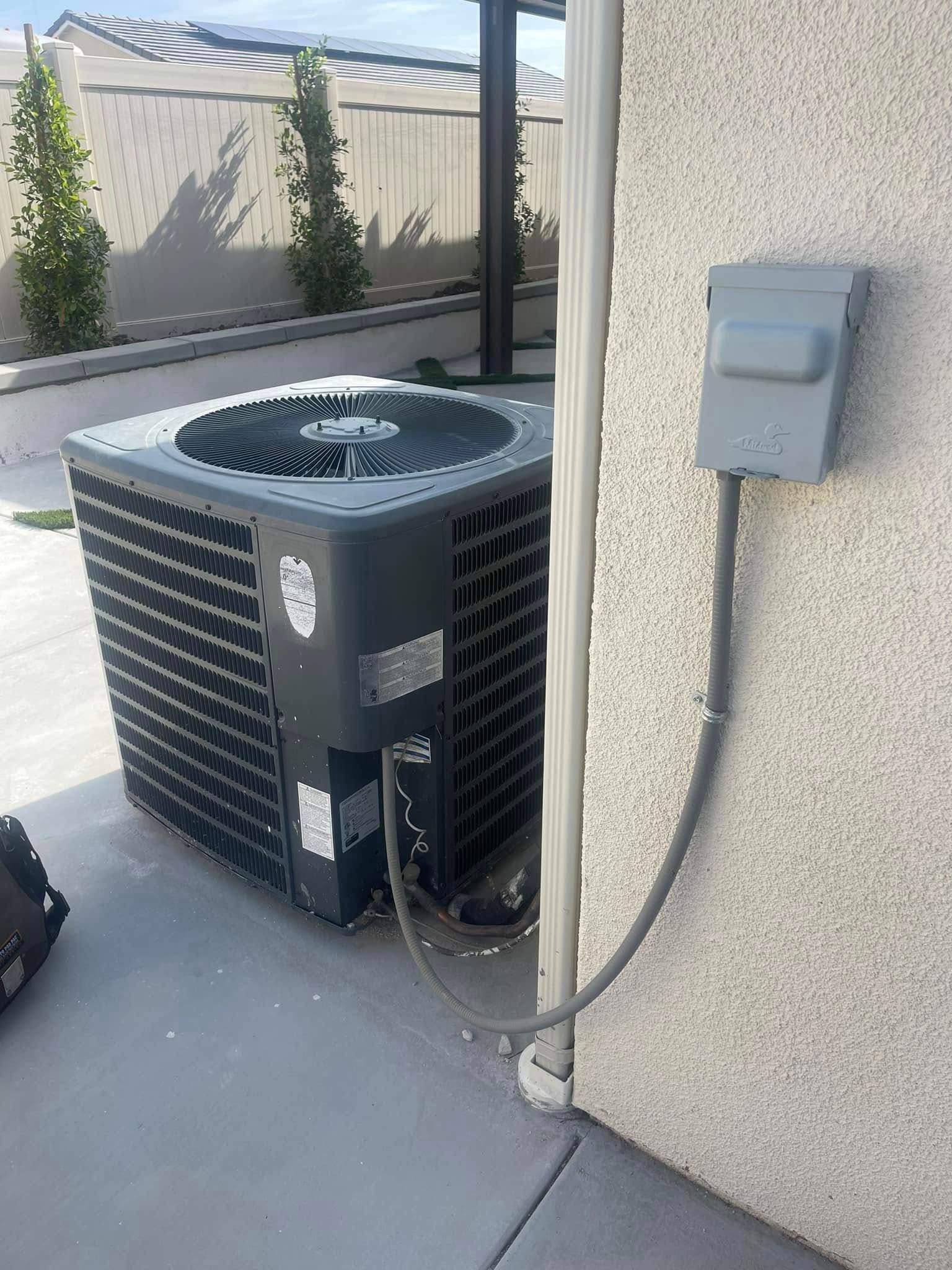 An outdoor air conditioning unit next to a light-colored wall with an electrical box.