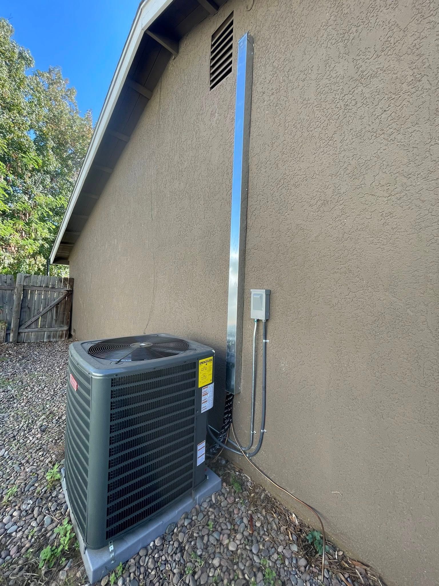 An air conditioning unit next to a stucco wall with a metal vent pipe and electrical conduit.