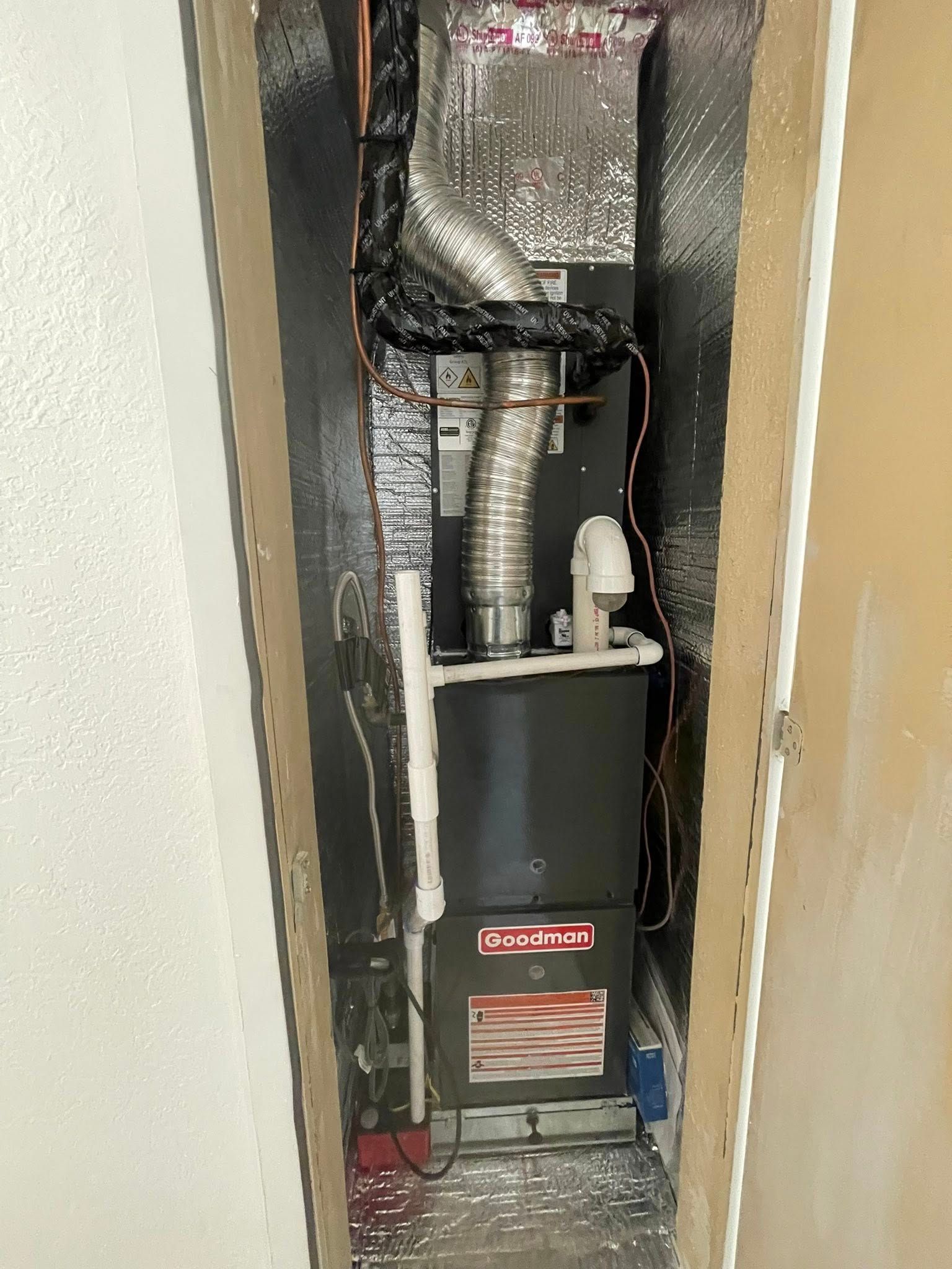 Furnace unit in a utility closet with silver insulation, exhaust pipe, and ductwork.