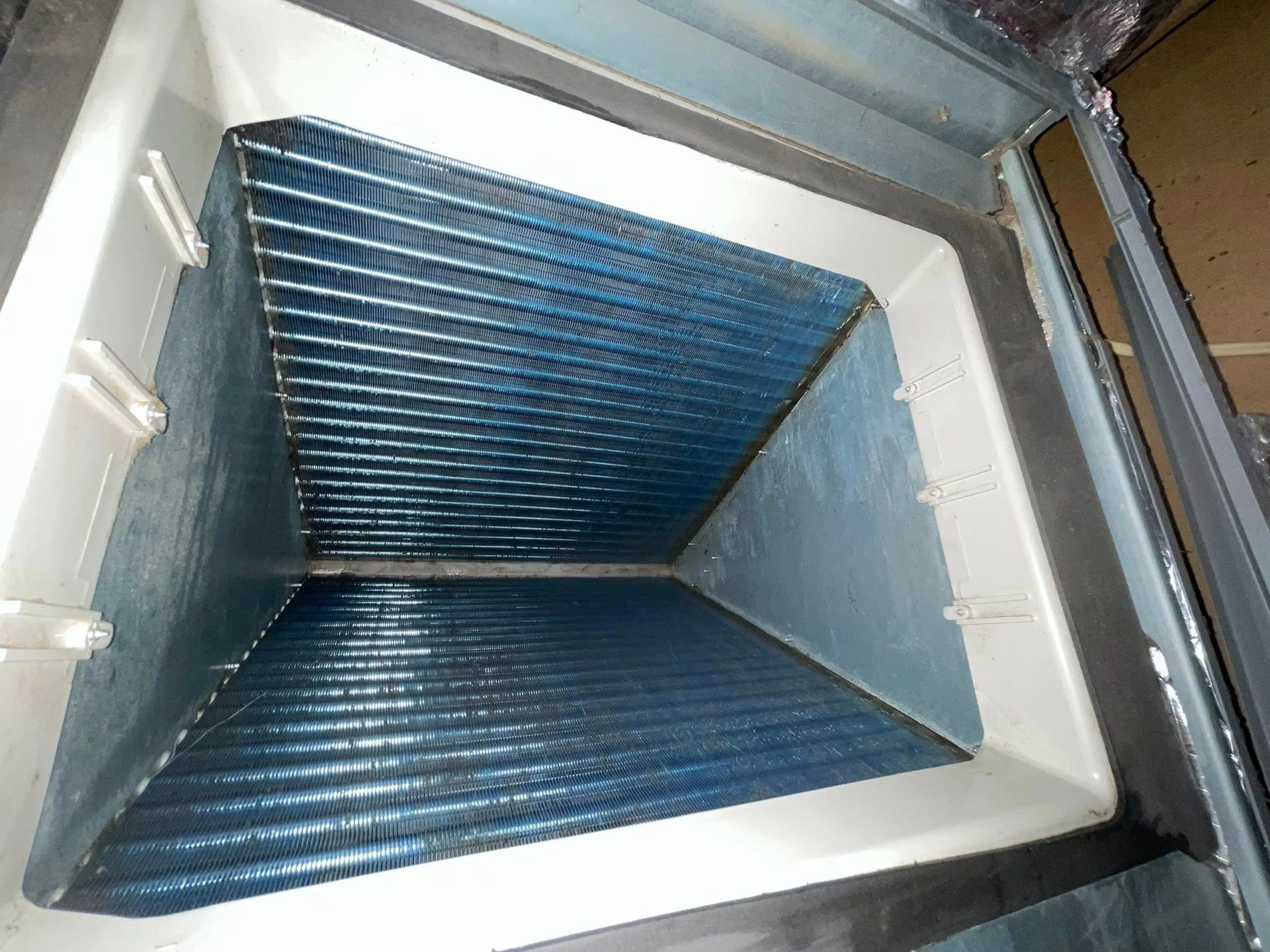 HVAC cooling coil inside a metal housing, blue fins, angled, white and silver interior.