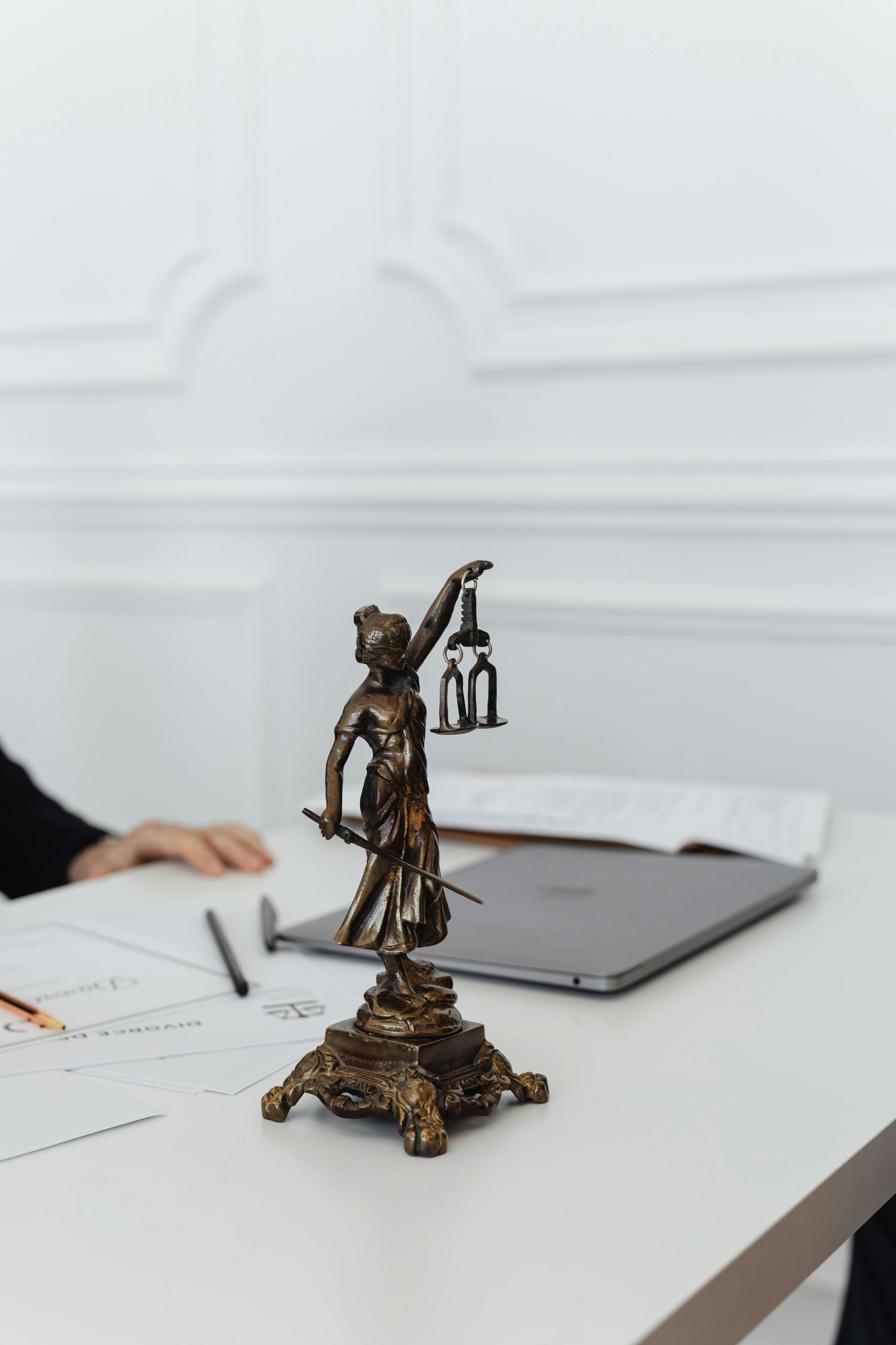 A statue of justice is sitting on a table next to a laptop.