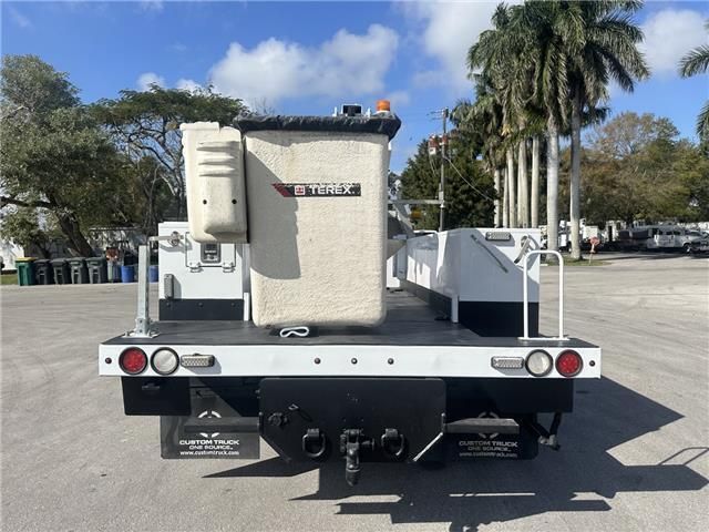 A white truck with a bucket on the back is parked in a parking lot