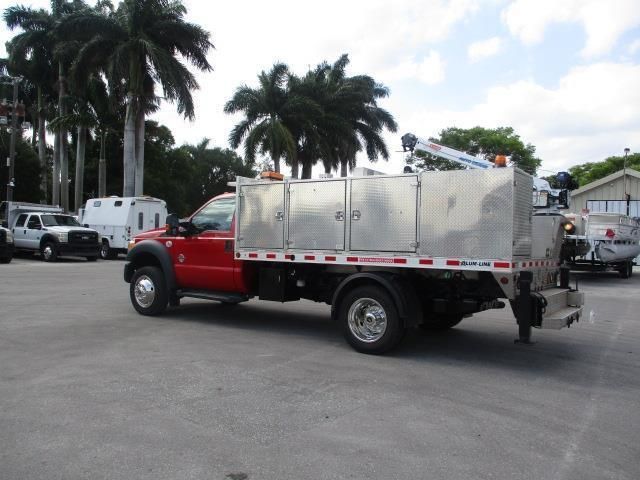 A red truck is parked in a parking lot with palm trees in the background