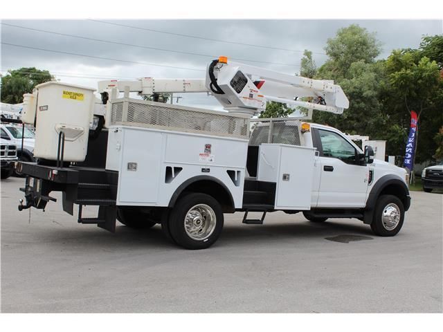A white utility truck with a crane on the back is parked in a parking lot.