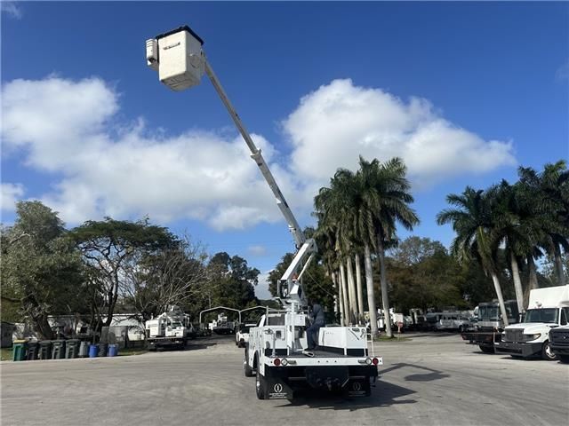 A white bucket truck is parked in a parking lot with palm trees in the background.