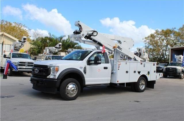 A white utility truck with a crane on the back is parked in a parking lot.