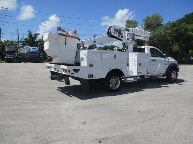 A white truck with a bucket on the back is parked in a parking lot.