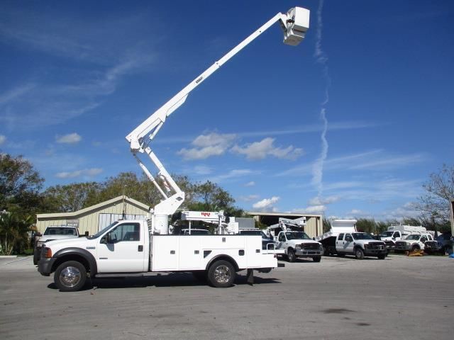 A white truck with a bucket on the back is parked in a parking lot.